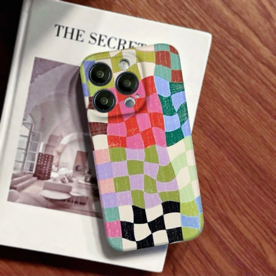A retro-inspired colorful plaid phone case lying on art magazine, highlighting the distressed texture and artistic vibe.
