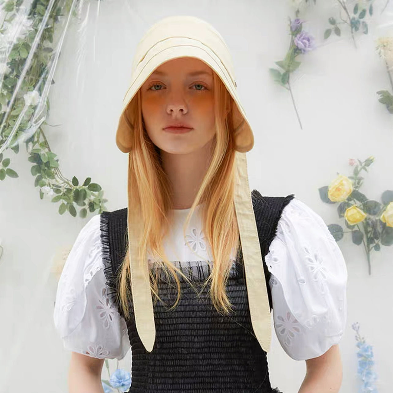 Model wearing the cream yellow ribbon hat in a bright outdoor garden setting.