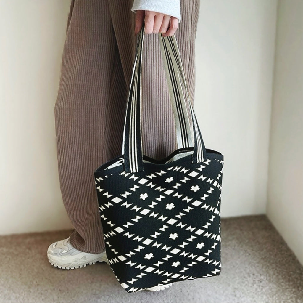 Model holding the black and white geometric bucket bag by the striped handle.