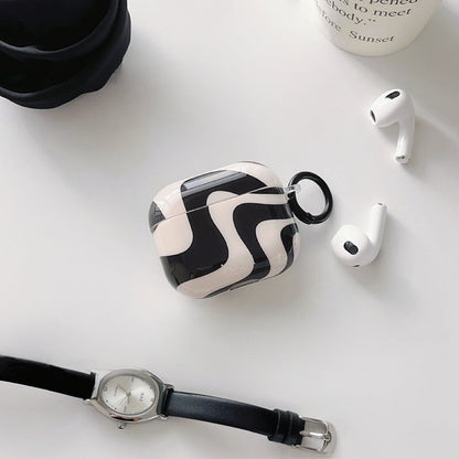 Front view of Black and white wavy silicone AirPods case cover with a black keyring, next to white AirPods.