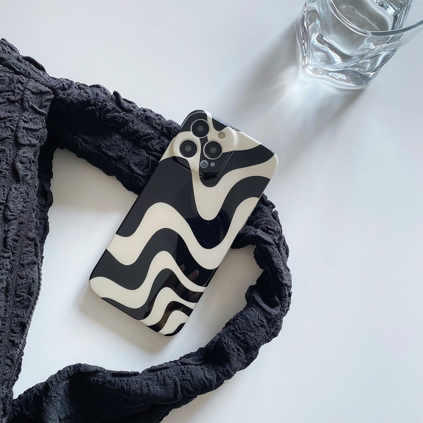 Abstract wavy acrylic phone case on white surface with strap. Aesthetic lifestyle flatlay for desk setup inspiration.