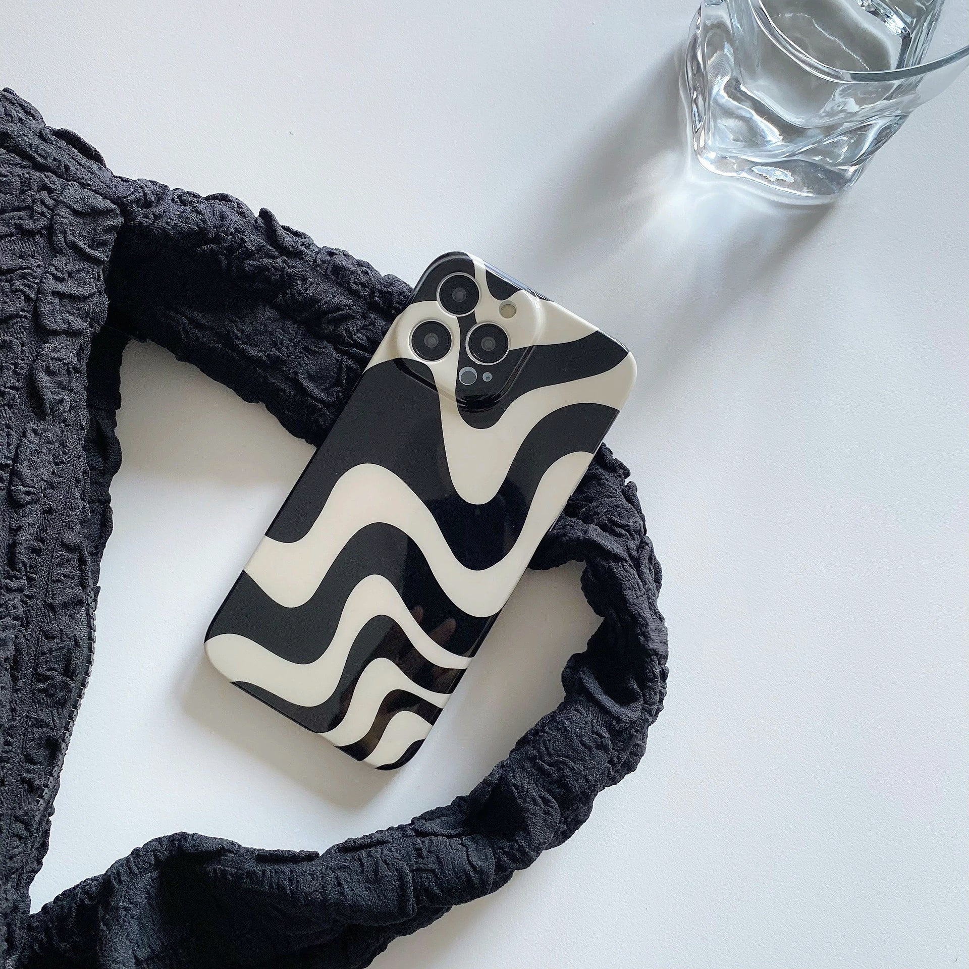 Abstract wavy acrylic phone case on white surface with strap. Aesthetic lifestyle flatlay for desk setup inspiration.