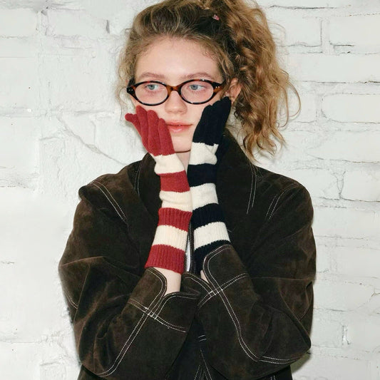 Model wearing bold stripe knit gloves, red/cream and navy/cream stripes; warm winter accessory for outdoors.