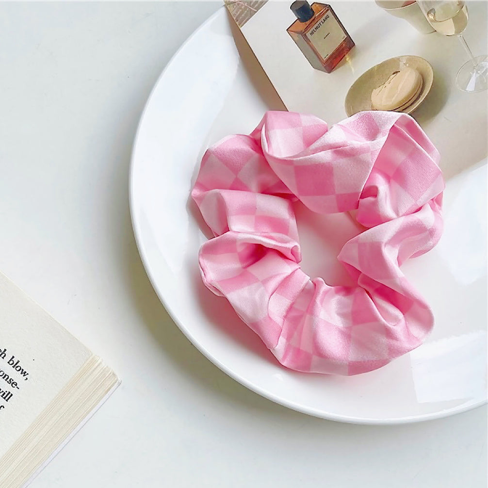 Angled view of checkerboard satin scrunchie in pink, great for everyday styling and gifting.