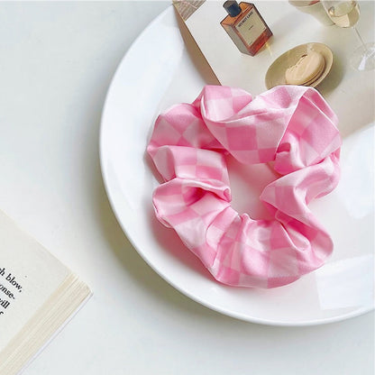Angled view of checkerboard satin scrunchie in pink, great for everyday styling and gifting.