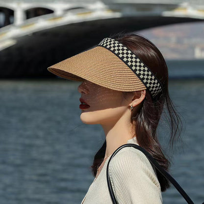 Straw visor hat with black and white checkered band worn by a woman in an outdoor setting.
