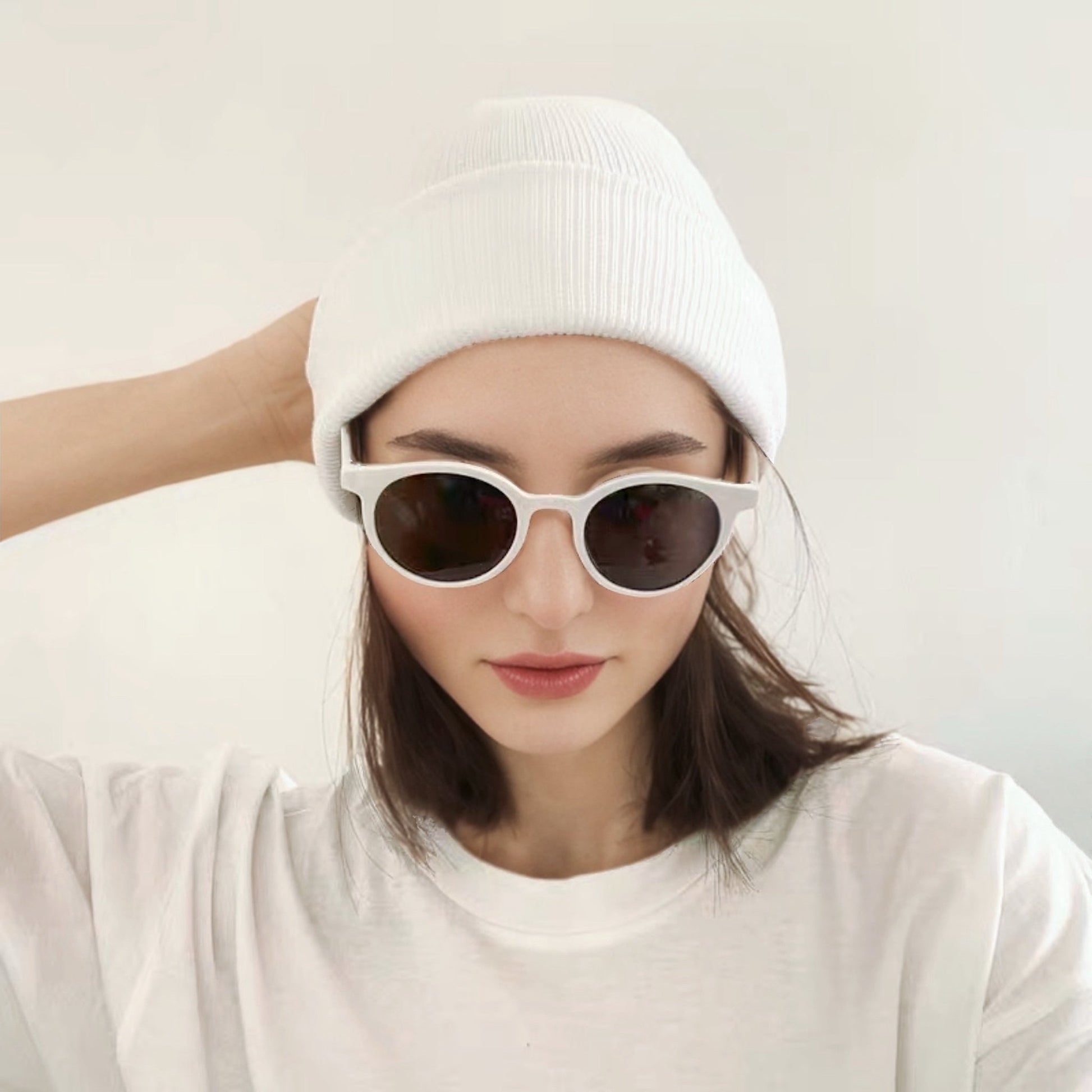 Woman wearing white knitted beanie with sunglasses, a chic accessory for urban winter street style.