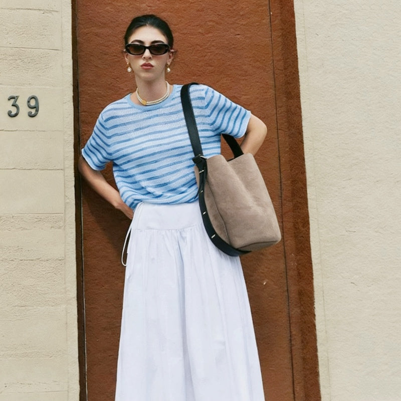 Model wearing the grey suede bucket bag as a short shoulder bag underarm.