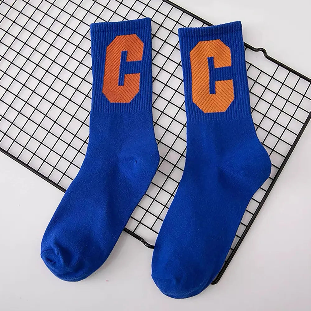 Angled view of  royal blue crew socks with a large orange C letter on each, made from cotton-acrylic blend.