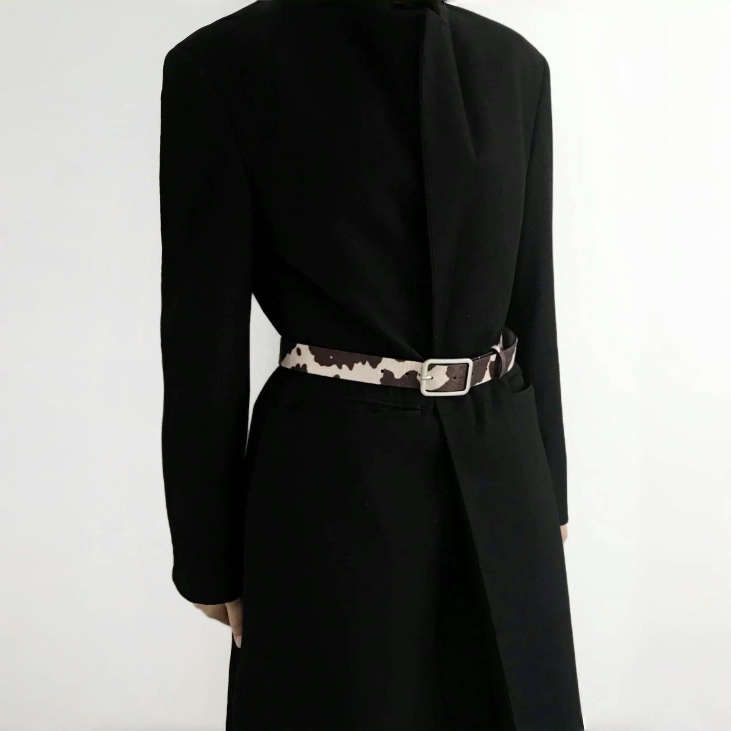 Model wearing a cow print furry belt over a black blazer; chic waist-cinching accessory perfect for office styling.