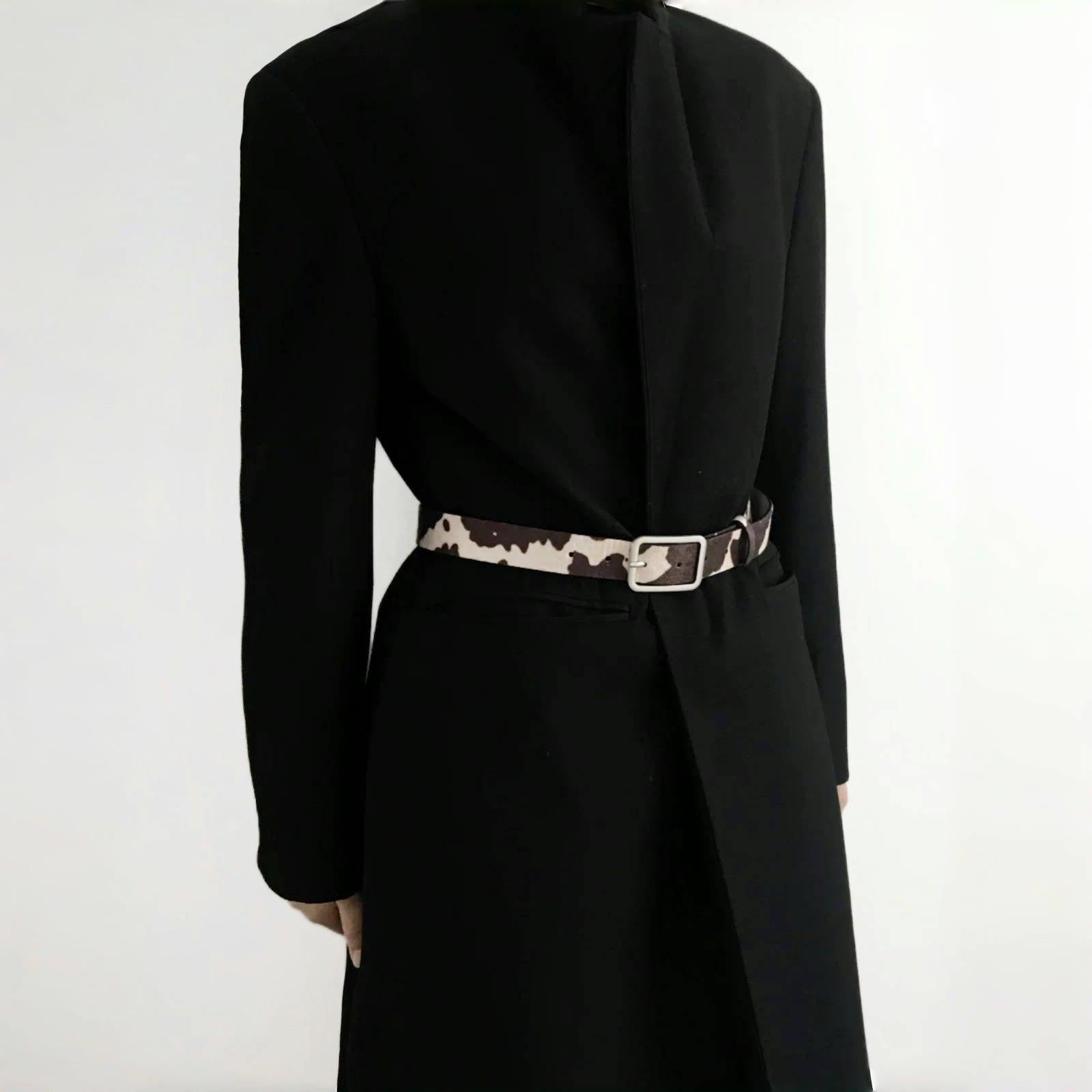 Model wearing a cow print furry belt over a black blazer; chic waist-cinching accessory perfect for office styling.