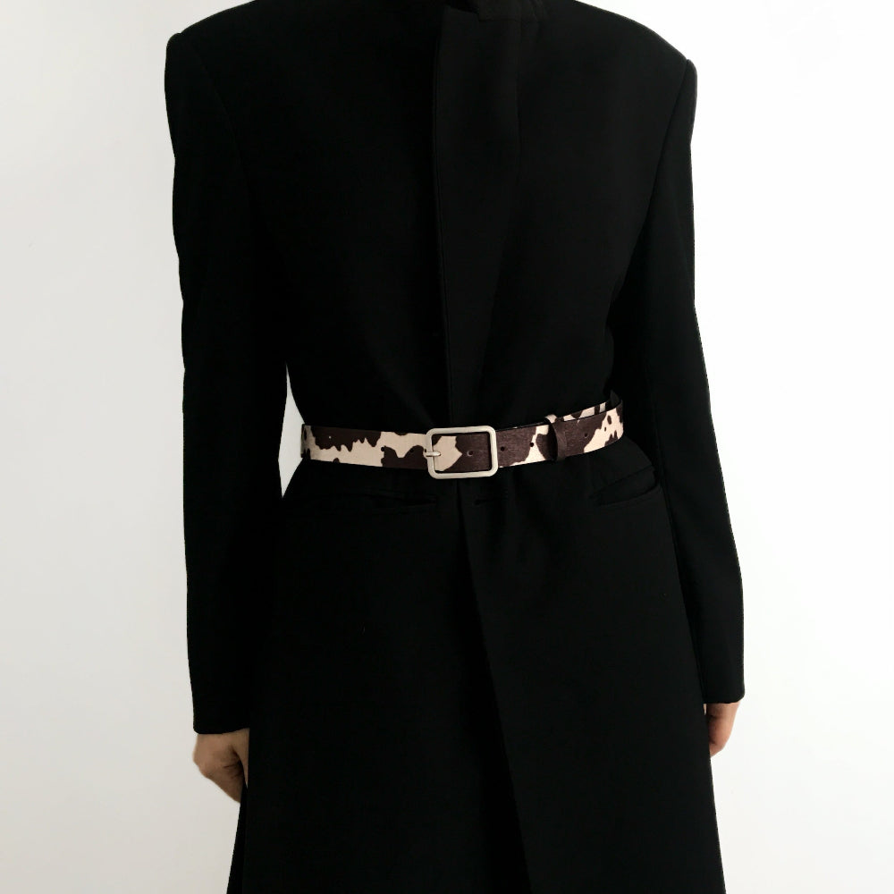 Close-up of cow print belt on a black coat; trendy animal print design suited for winter street style and layering.