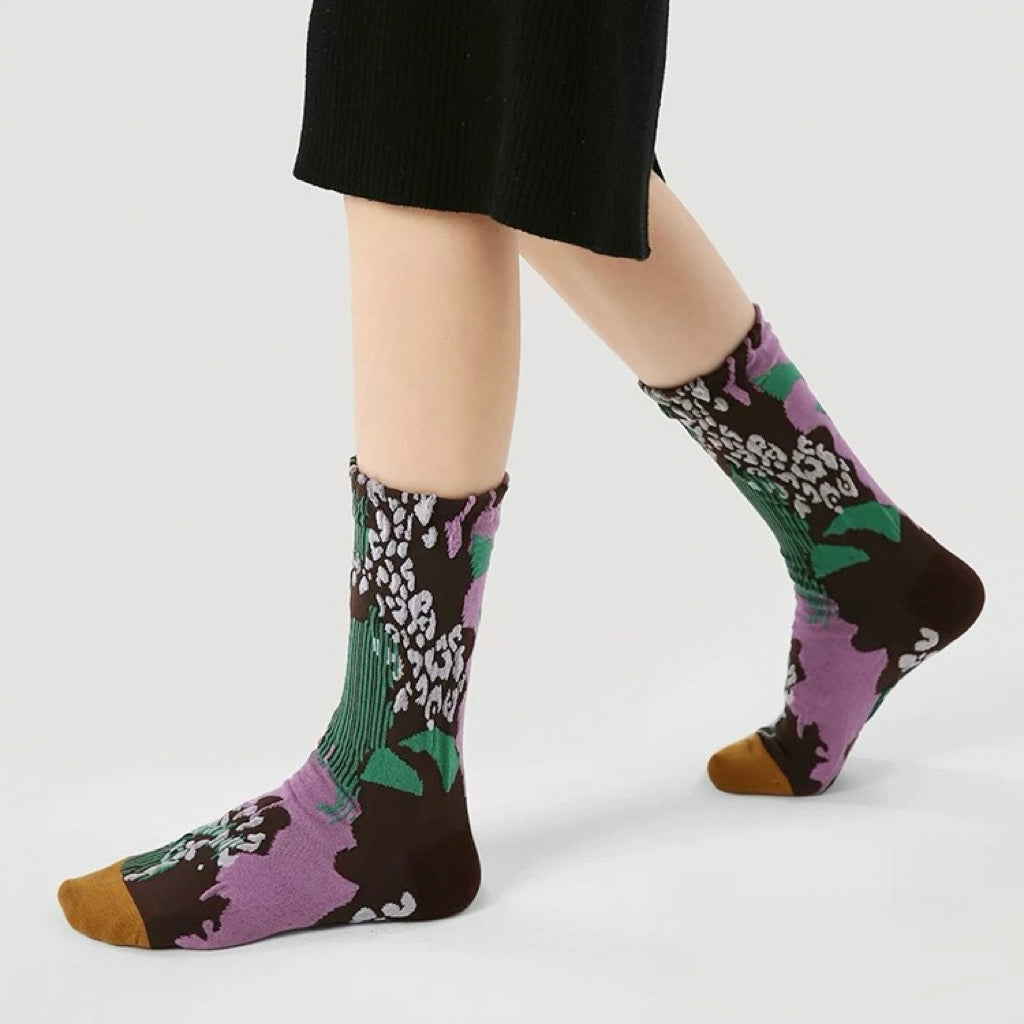 Model wearing a pair of Fantasy Garden  socks, with purple, brown, green, and white floral patterns.