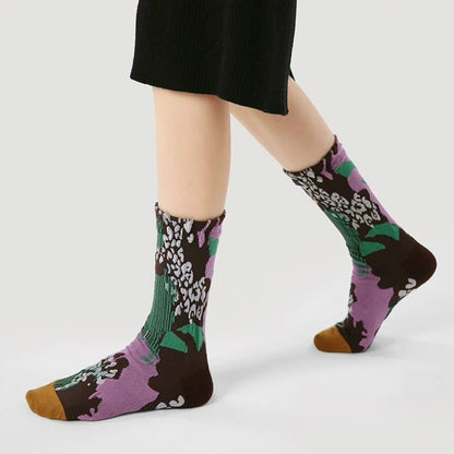 Model wearing a pair of Fantasy Garden  socks, with purple, brown, green, and white floral patterns.