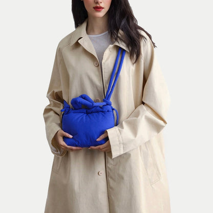 Model wearing the blue padded bag as crossbody with a beige trench coat, showcasing the innovative strap design.