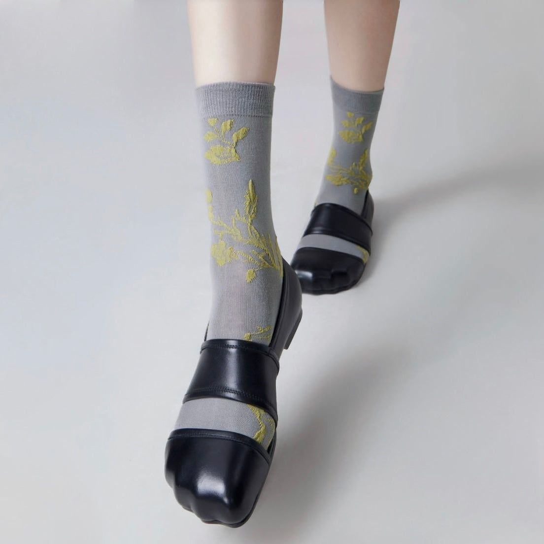 Model wearing a pair of Floral Embroidered Socks in gray, easy to pack for travel and errands.