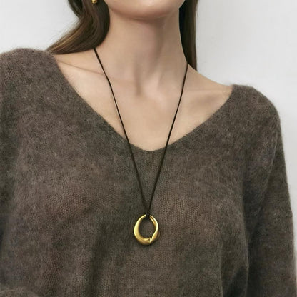 Model styling gold fluid oval pendant necklace with brown knitwear, minimalist aesthetic view