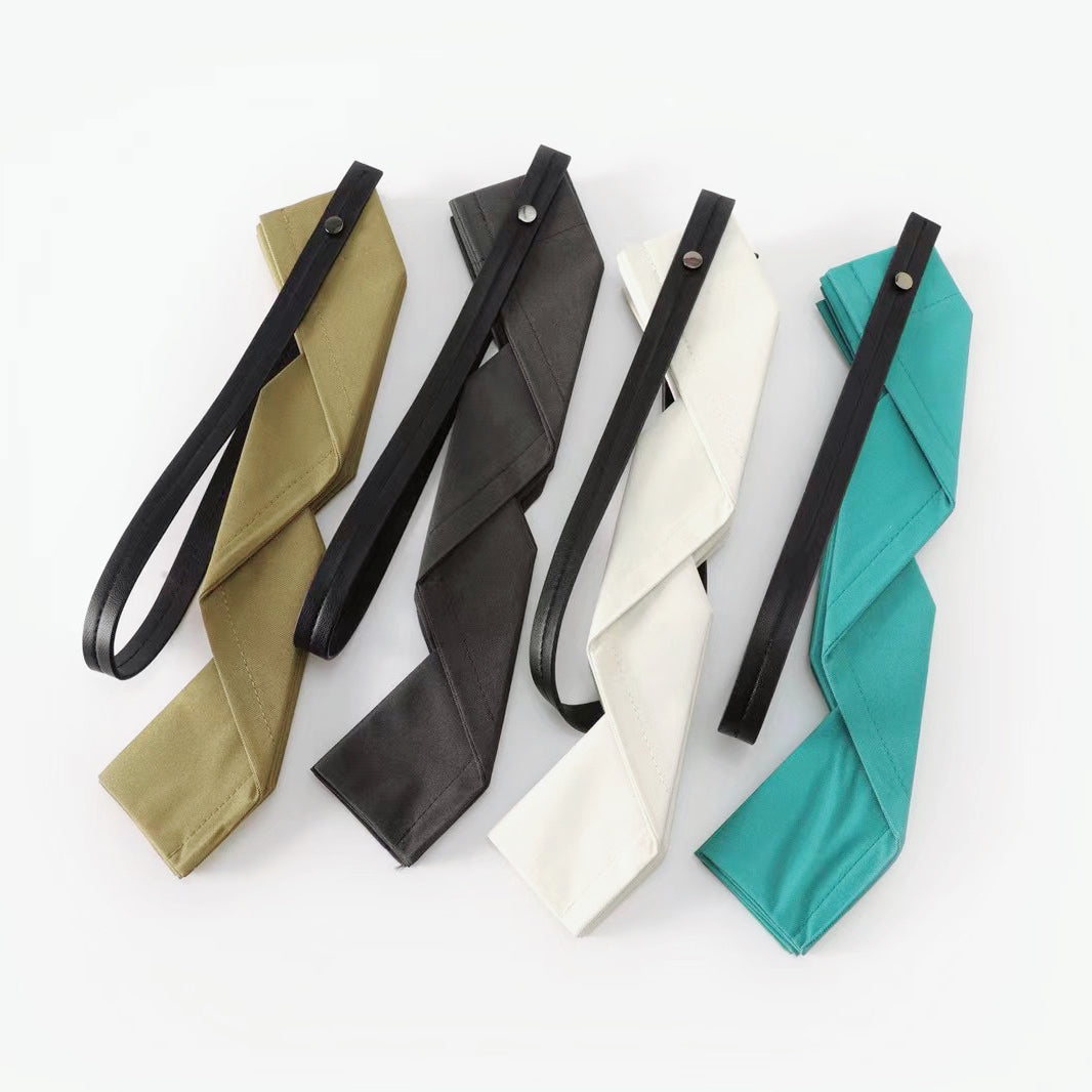 Four folded canvas pleated shopper bags in khaki, dark grey, white, and peacock blue with black straps.