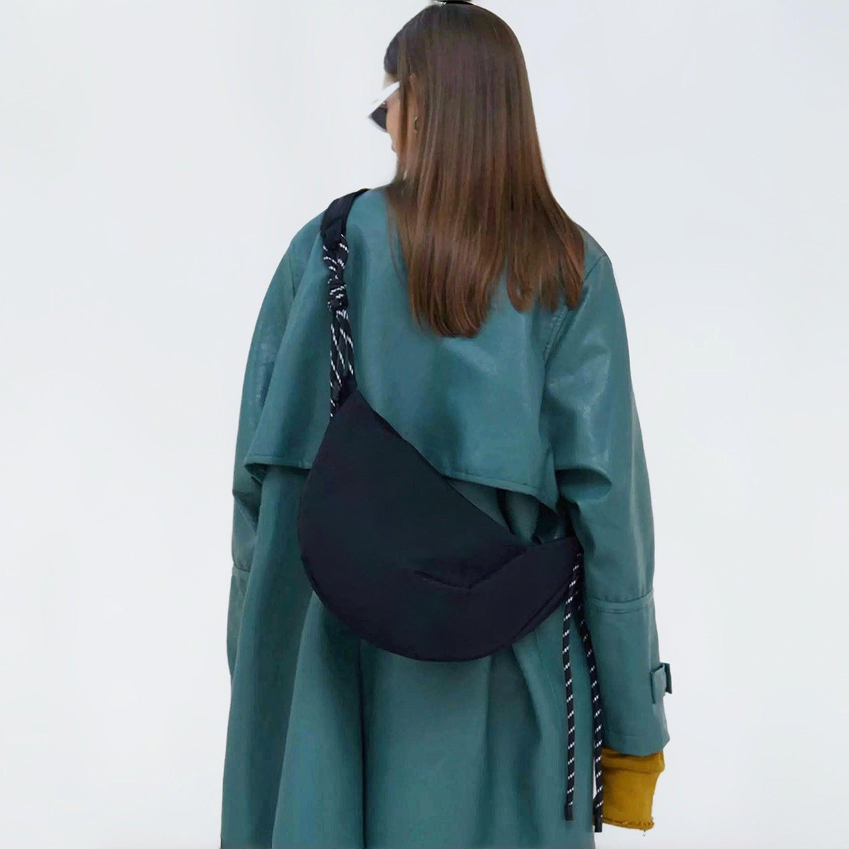 Black nylon crescent bag styled as a crossbody over a green oversized trench coat, showcasing a minimalist streetwear aesthetic.