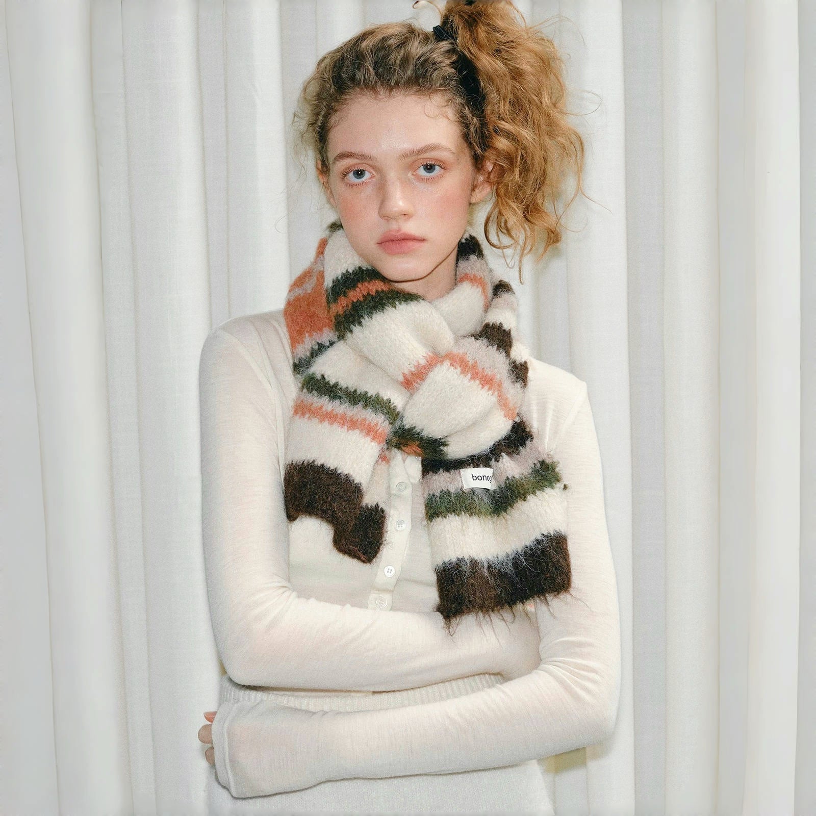 Model wearing Fuzzy wool-polyester striped scarf in earthy tones of cream, brown, green, and orange Fuzzy Nature.