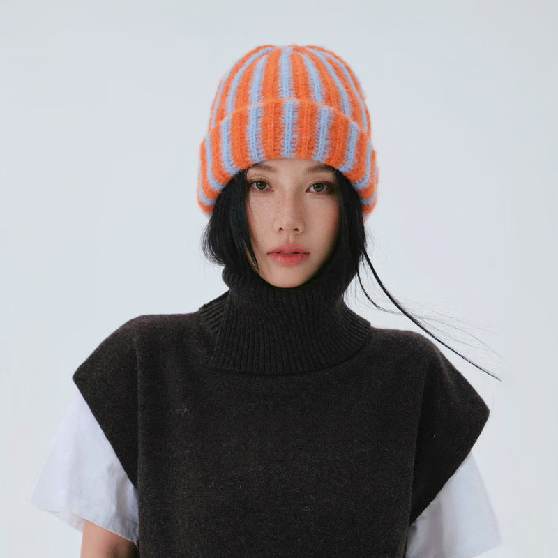Frontal view of a model in a dark vest wearing the orange blue striped beanie.