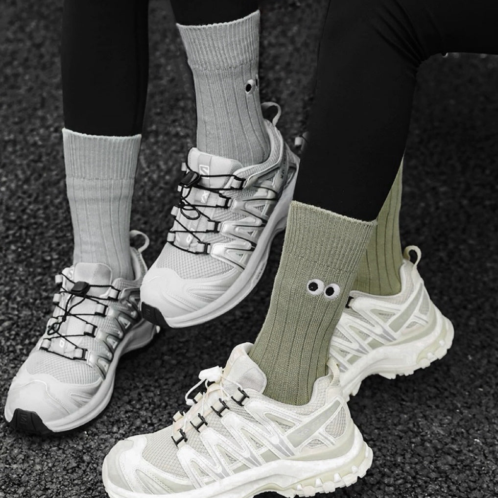 Two models wearing cotton googly eyes socks: one olive green and one grey.