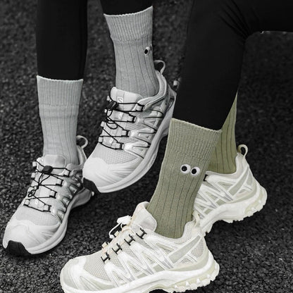 Two models wearing cotton googly eyes socks: one olive green and one grey.