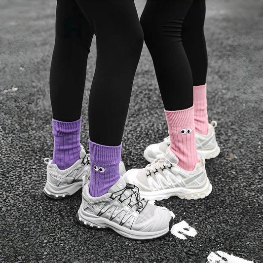 Two models wearing cotton googly eyes socks: one purple, one pink.