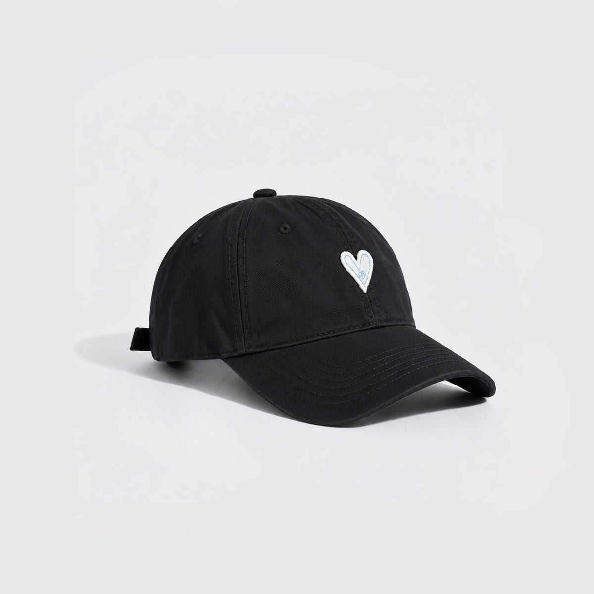 Side angle view of a classic black cotton twill cap featuring white heart embroidery.