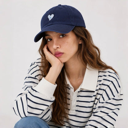 Model styling a navy blue heart embroidered dad hat with long brown hair.