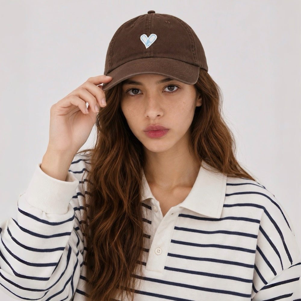 Model wearing a chocolate brown heart embroidered cap paired with a preppy striped polo shirt.