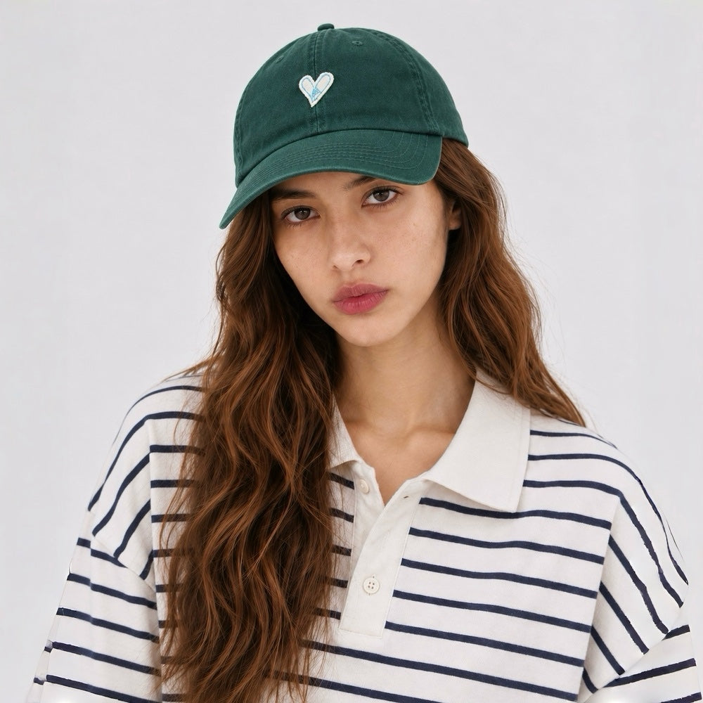 Model wearing a forest green cotton baseball hat with a white heart accent.