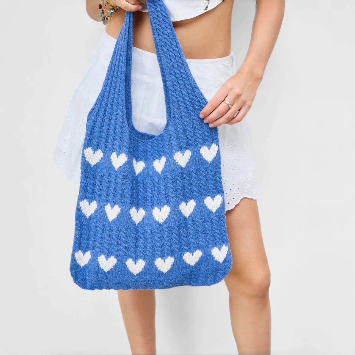 Model carrying a blue crochet tote bag with white heart pattern, made from blended knitting yarn.