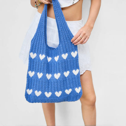 Model carrying a blue crochet tote bag with white heart pattern, made from blended knitting yarn.