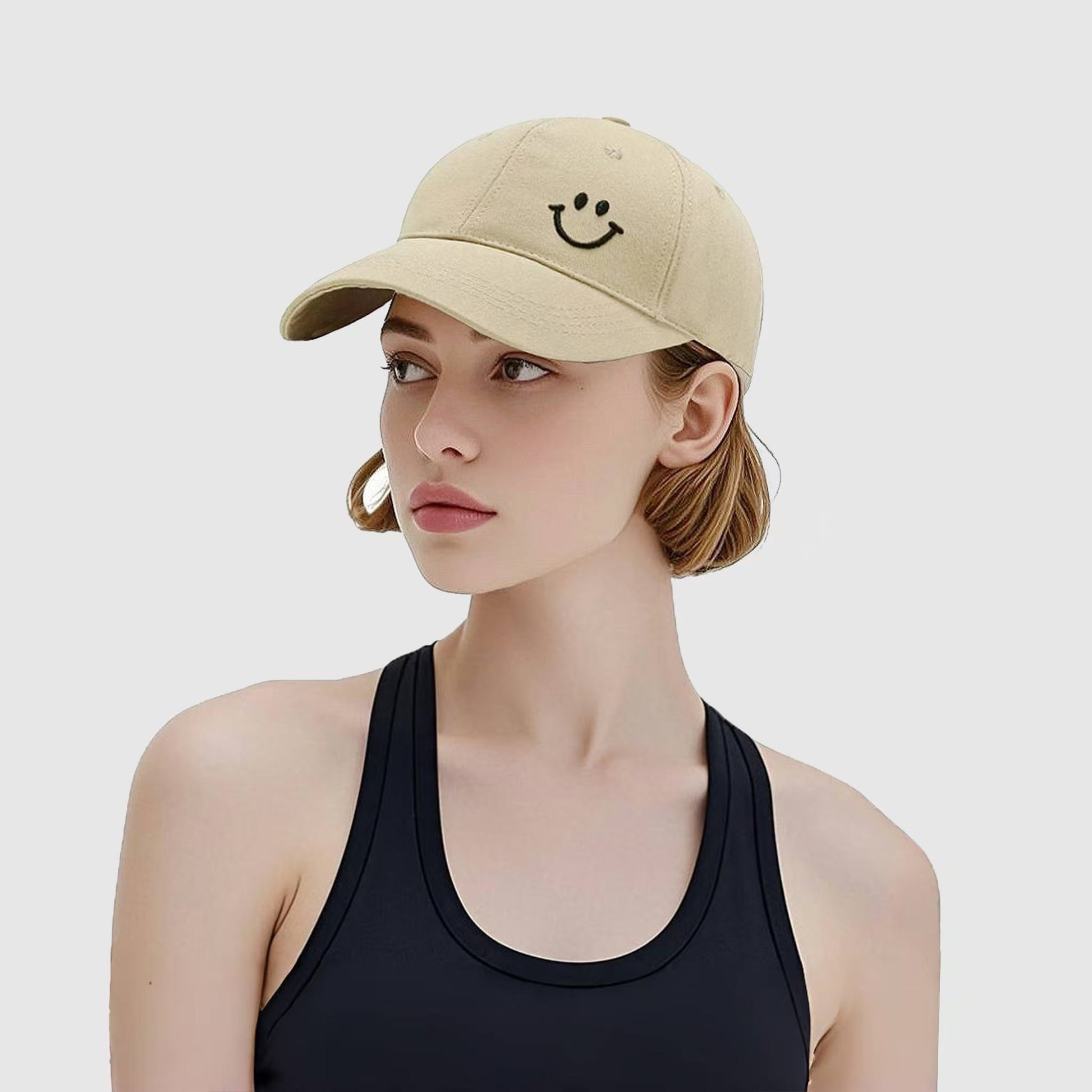Model wearing Joyful Grin Cap in beige, displays iconic smile graphic for a subtle yet playful everyday accessory.