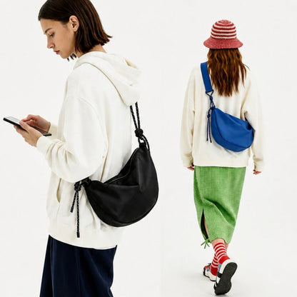 Two models wearing black and cobalt blue knotted crescent bags, showcasing the urban utility aesthetic.
