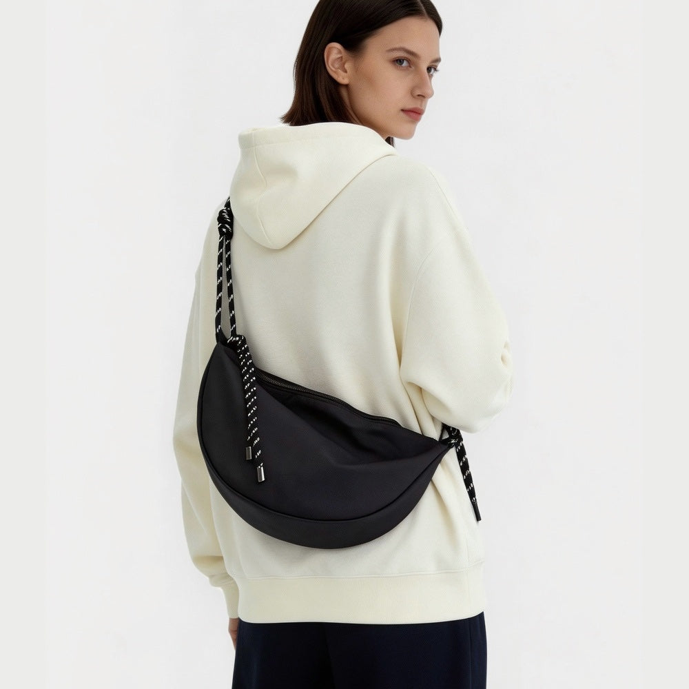 Model wearing a black nylon crescent sling bag over a white hoodie, large hobo bag for everyday carry.