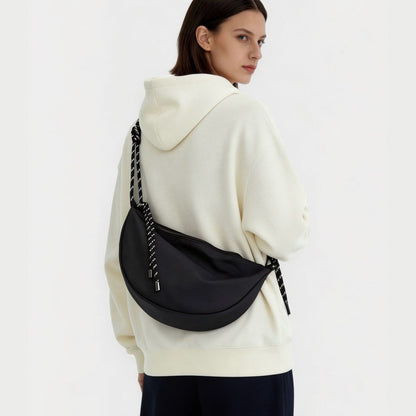 Model wearing a black nylon crescent sling bag over a white hoodie, large hobo bag for everyday carry.