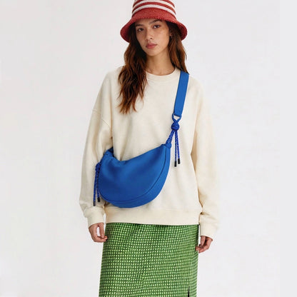 Model wearing a vibrant blue crescent bag, trendy water-resistant crossbody for iPad and essentials.