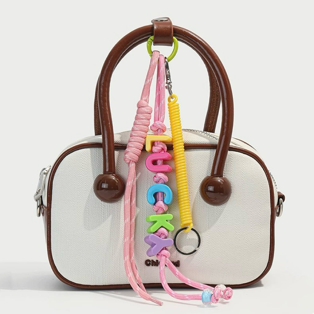 Pink Letters Bag Charm hanging on a white handbag, great for daily style and travel days.