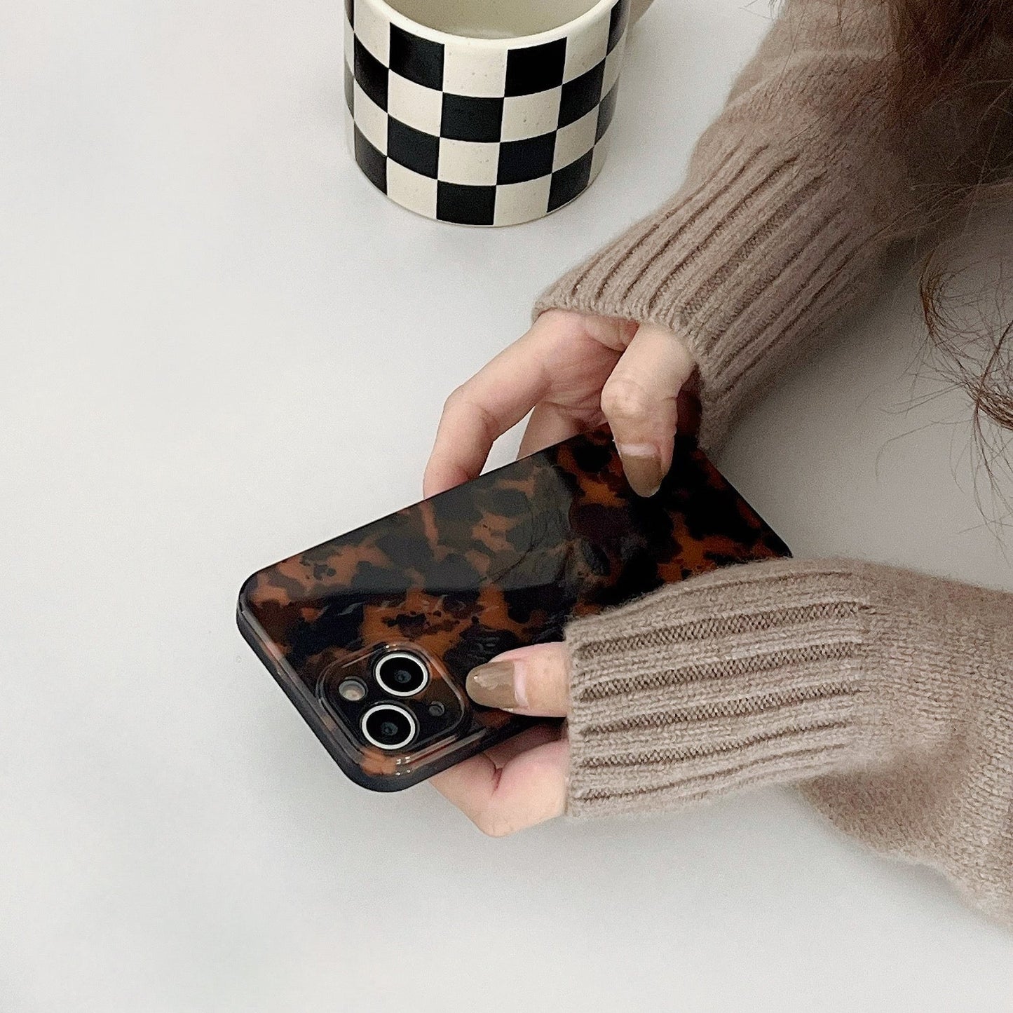 Hand in beige sweater holding Maillard Amber case. Warm tortoiseshell finish for cozy autumn fashion.