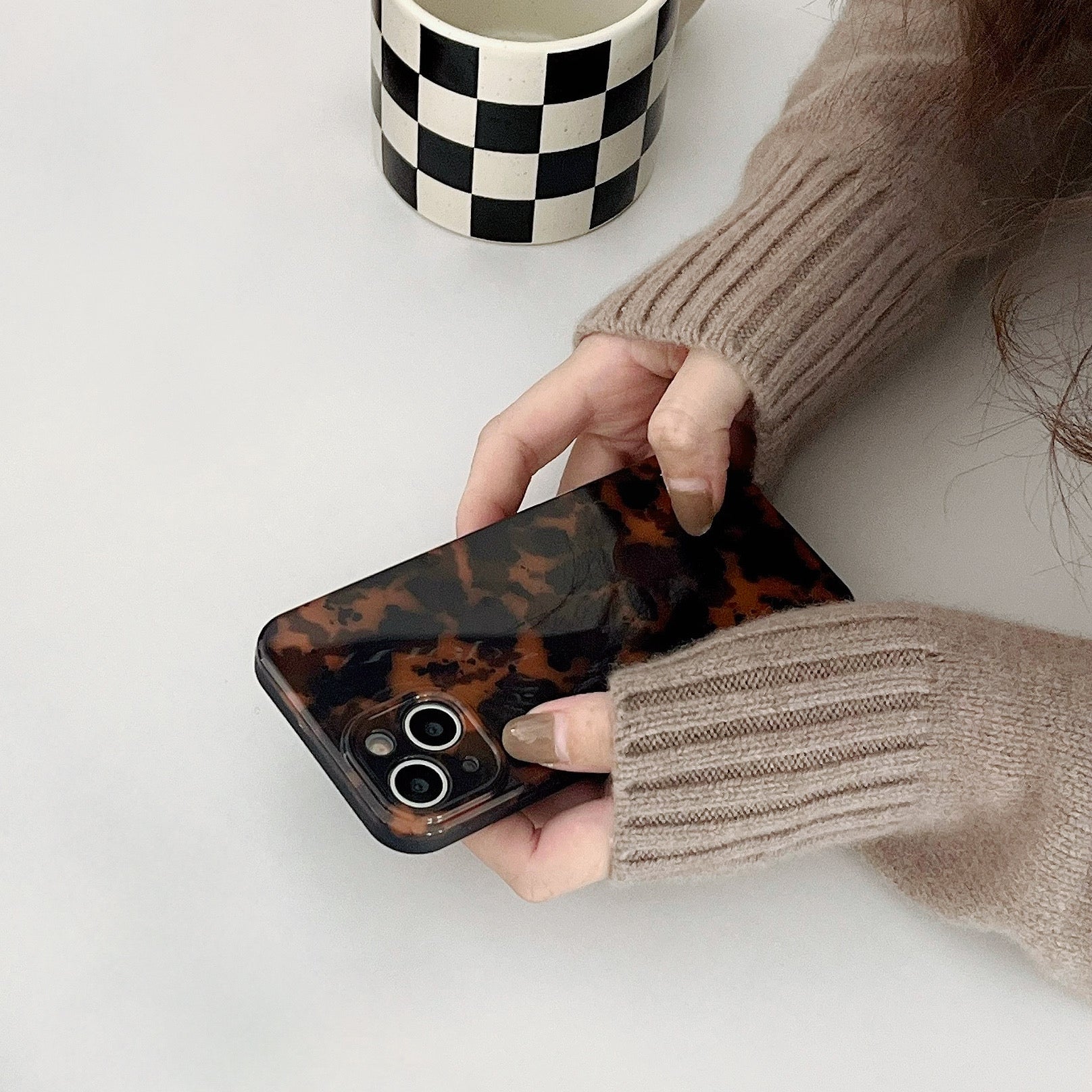 Hand in beige sweater holding Maillard Amber case. Warm tortoiseshell finish for cozy autumn fashion.