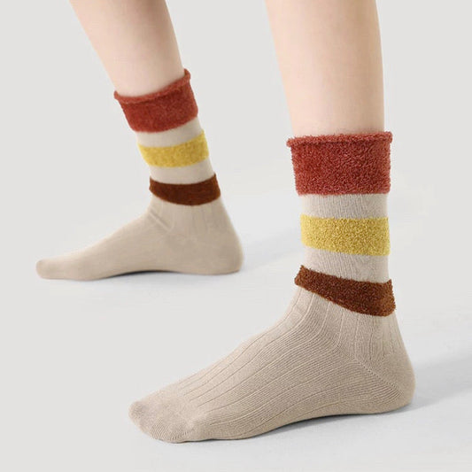 Model wearing a pair of Beige ribbed socks with plush red, yellow, and brown striped cuffs .