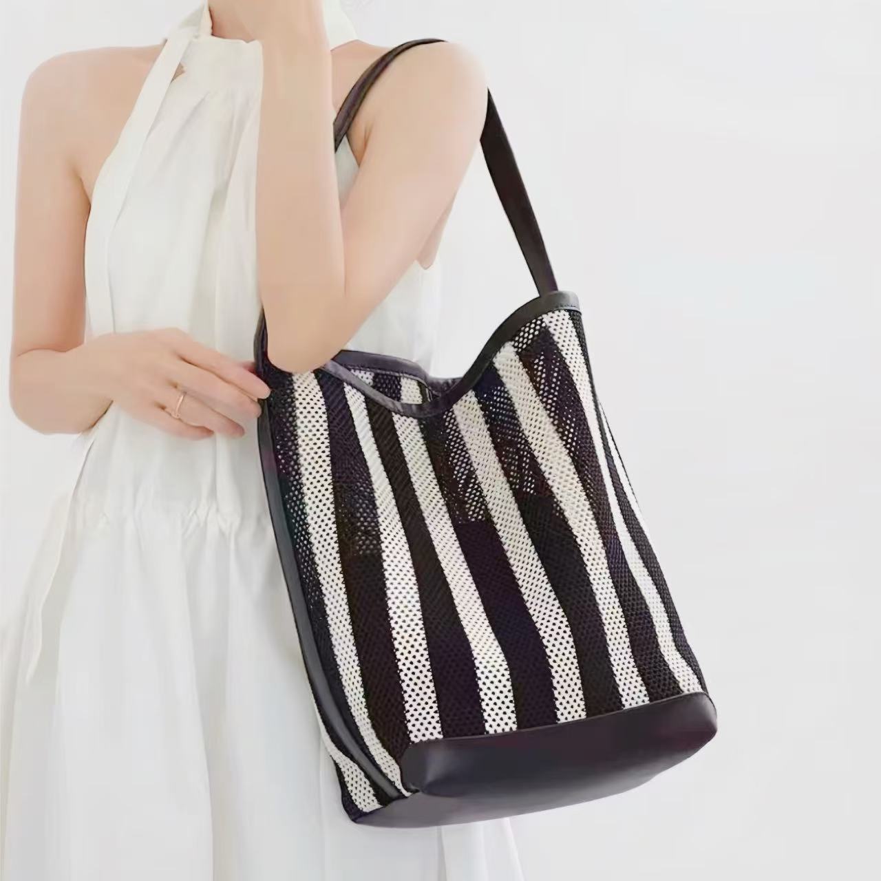 Close-up of a model carrying the large striped mesh shoulder bag with heavy-duty black leather trim.