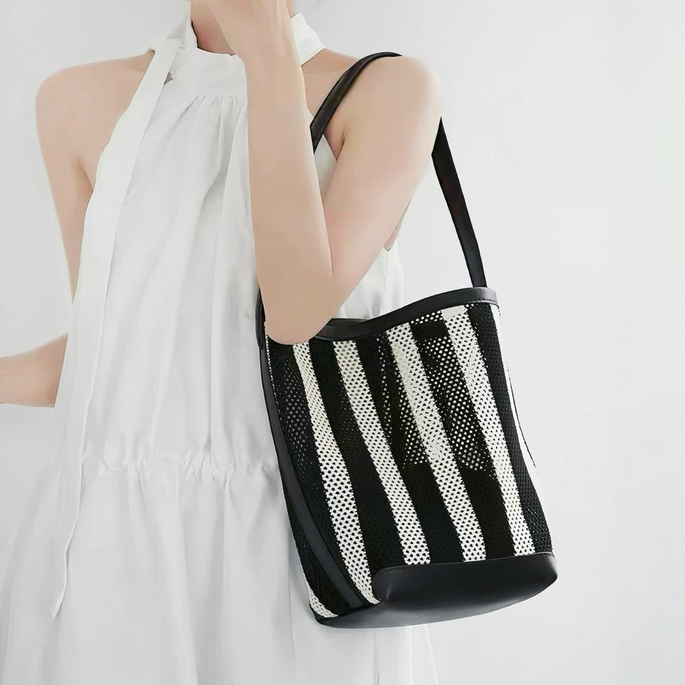 Model styling the small size monochrome striped mesh tote pouch under the arm showcasing the black PU leather strap.