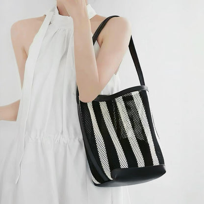 Model styling the small size monochrome striped mesh tote pouch under the arm showcasing the black PU leather strap.
