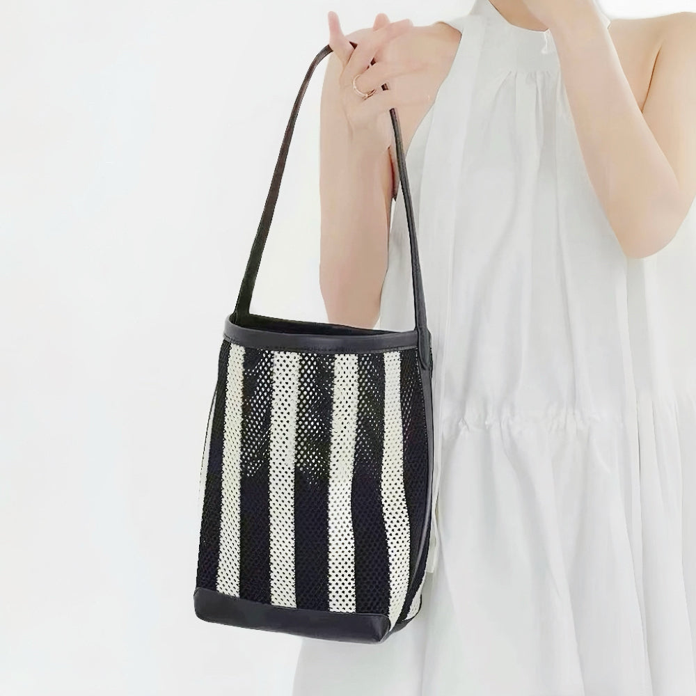 model holding the small monochrome mesh tote sling, displaying its deep vertical black and white structural panels.