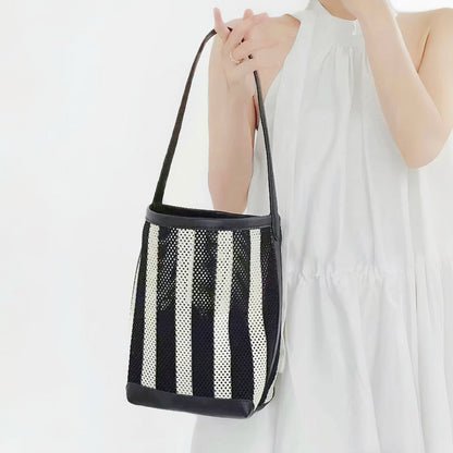 model holding the small monochrome mesh tote sling, displaying its deep vertical black and white structural panels.