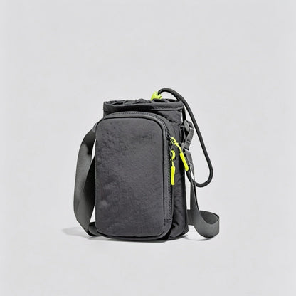 Studio flat lay of the dark grey multi-way nylon bottle carrier featuring its front zippered phone compartment.