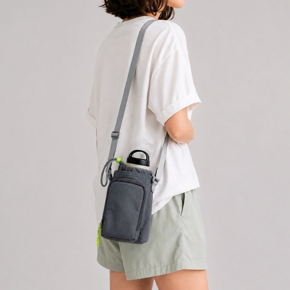 Back view of a model showcasing how the dark grey nylon bottle sling bag sits comfortably flat against the lower back.